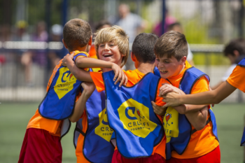 Jongens in oranje shirt met Cruyff Court hesjes in blauw geel omhelzen elkaar