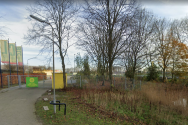 Een oprit naar het voetbalveld toe met groen en geel gekleurde vlaggen