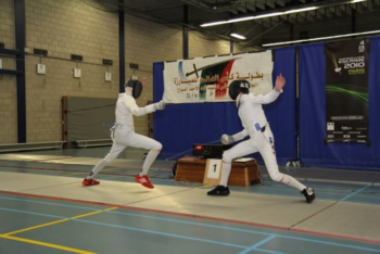 Twee personen spelen de sport Schermen tegen elkaar op een grote grijze mat.