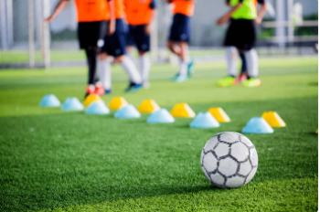 Een voetbal op een grasveld met achterin benen van verschillende personen