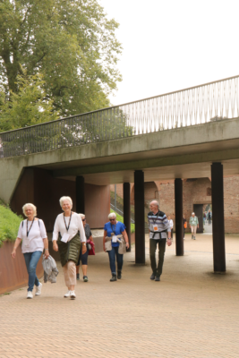 Drie dames en een heer wandelend onder een brug