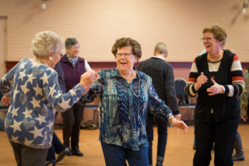 Drie dames die dansend in een zaal staan met de handen in elkaar