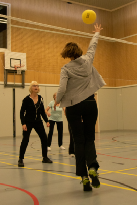 Sportende vrouw in een gymzaal speelt de bal over het volleybalnet.